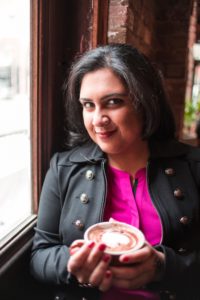 Head shot of author Nisha Sharma holding a cup of cappucino