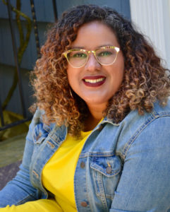 Headshot of Adriana Herrera wearing a yellow shirt and a denim jacket